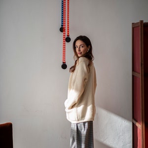 Relaxed silhouette winter sweater with a V-neckline, raglan sleeves, front pockets, and a button closure. Made of New Zealand Merino wool