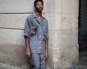May include: A person wearing a gray linen shirt and matching pants. The person is standing against a gray wall.