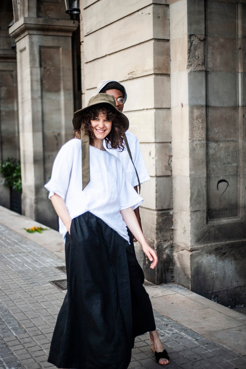 Minimalist linen outfit of a white T-shirt and black wide-leg trousers with pockets and an elastic waistband.