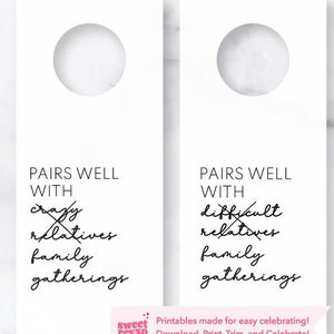 Puede incluir: Dos etiquetas de botella de vino blancas imprimibles con texto negro que dice "Combina bien con" y enumera opciones como "familiares locos" y "familiares difíciles". El texto está tachado en las etiquetas. Las etiquetas están sobre un fondo de mármol.