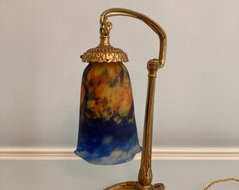 May include: A gold-toned table lamp with a blue and yellow glass shade. The lamp has a curved arm and a decorative base.