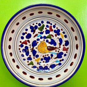 May include: A white ceramic bowl with a blue rim and a hand-painted design of a yellow bird with brown wings and blue flowers on a white background.