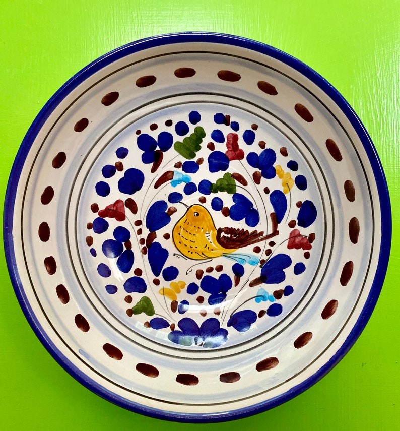 Pode incluir: Uma tigela de cer&acirc;mica branca com uma borda azul e um desenho pintado &agrave; m&atilde;o de um p&aacute;ssaro amarelo com asas marrons e flores azuis sobre um fundo branco.