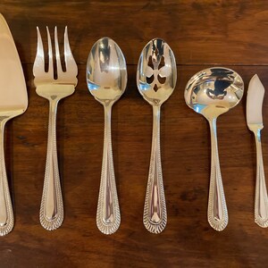 May include: A set of six silver-plated serving utensils, including a cake server, a serving fork, a serving spoon, a slotted spoon, a ladle, and a butter knife. The utensils have a beaded design on the handles.