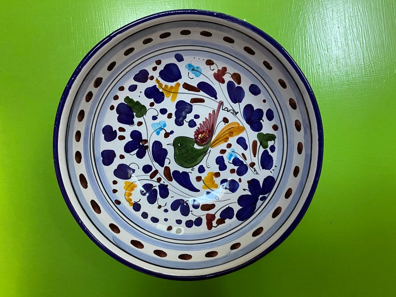Pode incluir: Uma tigela de cer&acirc;mica branca com uma borda azul e um desenho floral azul, verde, amarelo e castanho com um p&aacute;ssaro. A tigela tem um fundo branco com uma borda azul e branca.