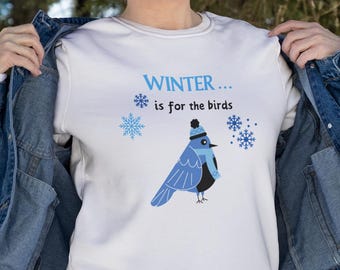 Op de afbeelding: Wit sweatshirt met een blauwe vogel die een blauwe muts en sjaal draagt. De tekst op het shirt luidt "WINTER... is for the birds".