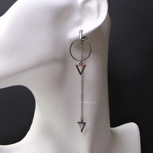 Peut inclure: Une boucle d'oreille en argent avec une chaîne pendante et deux breloques triangulaires. La chaîne est attachée à la boucle et a un breloque triangulaire en bas. La boucle d'oreille est sur une tête de mannequin blanche.