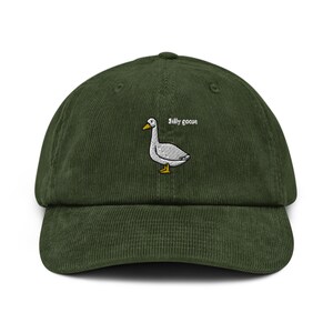 May include: A dark green corduroy baseball cap with a white embroidered goose and the text "silly goose". The goose has a yellow beak and feet. The cap has a curved brim and an adjustable strap.