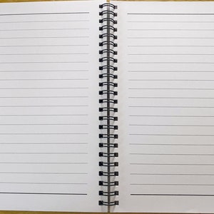May include: A white spiral bound notebook with lined pages. The notebook is open to a blank page.