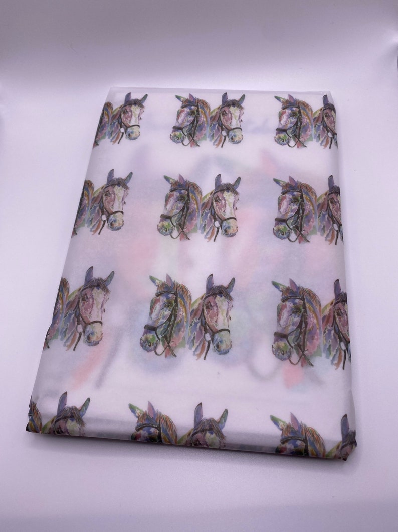 May include: White tissue paper with a repeating pattern of watercolour horse heads. The horses are brown and white with purple, blue, and green accents.