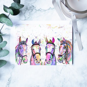 May include: A greeting card featuring a watercolour painting of four horses' heads. The horses are painted in shades of pink, blue, purple, and green, with splashes of colour in the background.