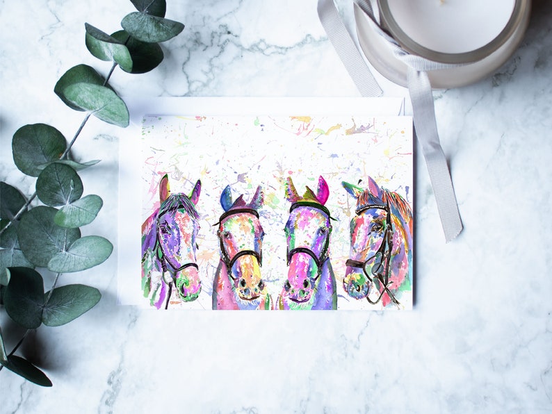 May include: A greeting card featuring a watercolour painting of four horses' heads. The horses are painted in shades of pink, blue, purple, and green, with splashes of colour in the background.
