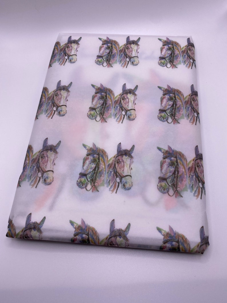 May include: White tissue paper with a repeating pattern of watercolour horse heads. The horses are brown with purple, blue, and green accents.