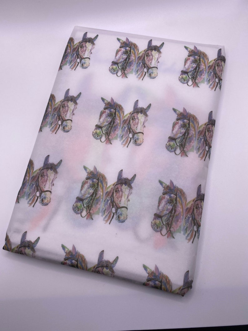 May include: White tissue paper with a repeating pattern of watercolour horse heads. The horses are facing forward and have brown, black, and white markings.