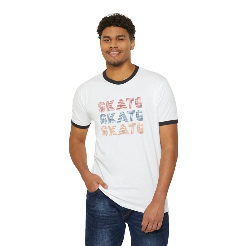 Op de afbeelding: Wit T-shirt met een zwarte boord en het woord "SKATE" drie keer herhaald in een retro-lettertype met rode, blauwe en oranje strepen.