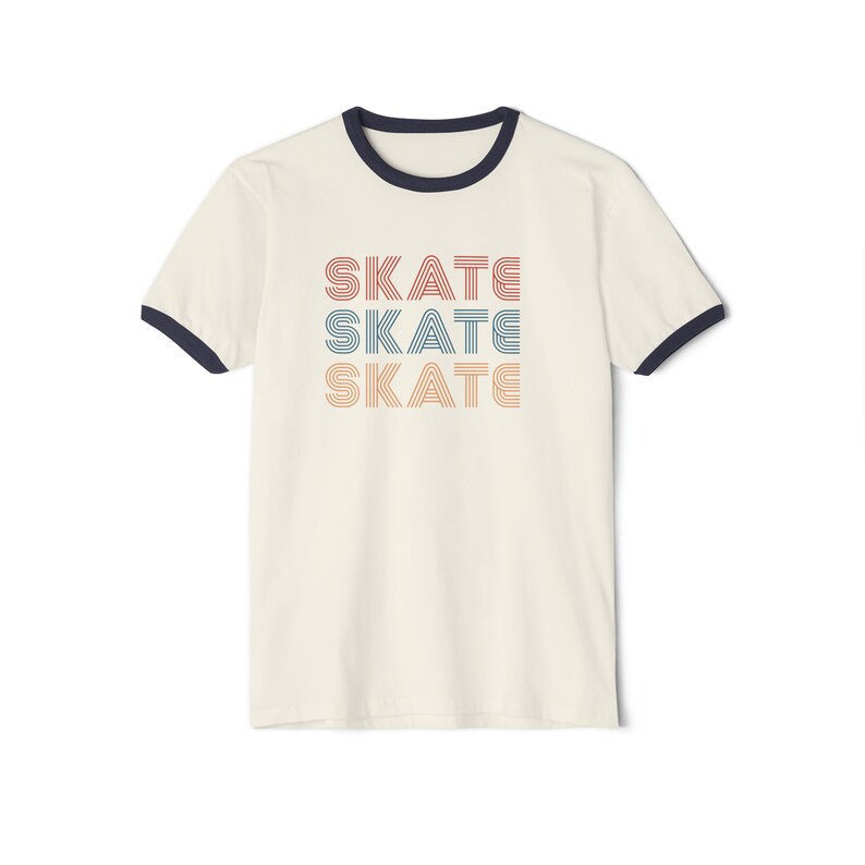 Op de afbeelding: Een wit T-shirt met een marineblauwe boord. Het shirt heeft een grafische afbeelding van het woord "SKATE" dat drie keer wordt herhaald in een retro-lettertype met de kleuren rood, oranje en blauw.