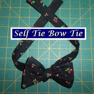 May include: A black self-tie bow tie with a cherry print. The bow tie has a hook and loop fastener for easy adjustment.