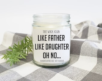 May include: A white soy candle in a clear glass jar with a black and white label that reads "The Wick Club Like Father Like Daughter Oh No... Handcrafted 8 oz Soy Candle".