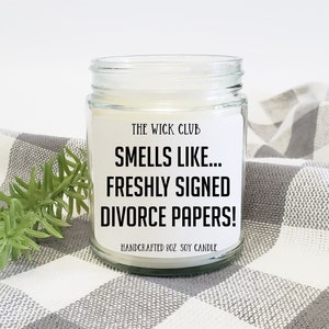 Puede incluir: Una vela de vidrio en un frasco con una etiqueta blanca que dice "THE WICK CLUB SMELLS LIKE... FRESHLY SIGNED DIVORCE PAPERS! HANDCRAFTED 8OZ SOY CANDLE".