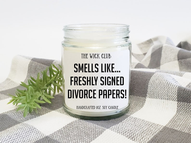 Puede incluir: Una vela de vidrio en un frasco con una etiqueta blanca que dice "THE WICK CLUB SMELLS LIKE... FRESHLY SIGNED DIVORCE PAPERS! HANDCRAFTED 8OZ SOY CANDLE".