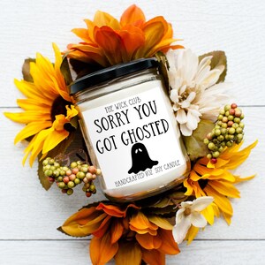 Peut inclure: Une bougie en soja blanche avec une étiquette noire sur laquelle est inscrit "The Wick Club Sorry You Got Ghosted" avec un dessin de fantôme. La bougie est entourée de fleurs aux couleurs d'automne.