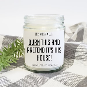 May include: A white soy candle in a clear glass jar with a black label that reads "THE WICK CLUB BURN THIS AND PRETEND IT'S HIS HOUSE! HANDCRAFTED 8OZ SOY CANDLE".