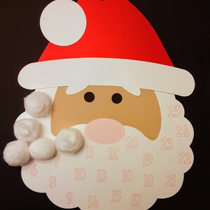 Puede incluir: Una cara de Papá Noel de papel blanco con un gorro rojo y una barba blanca. La barba tiene bolas de algodón pegadas y la cara tiene los números del 1 al 25 impresos.