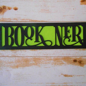 K&ouml;nnte beinhalten: Schwarzer und gr&uuml;ner Lesezeichen mit den ausgeschnittenen Worten "BOOK NERD", die einen gr&uuml;nen Hintergrund freilegen.