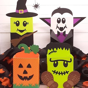 May include: Four Halloween-themed treat boxes. A witch with a black hat and broom, a vampire with fangs, a pumpkin with a jack-o-lantern face, and a Frankenstein monster with green skin and stitches.