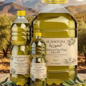 Puede incluir: Tres botellas transparentes de aceite de oliva con tapas amarillas y etiquetas que dicen "AL HAOUZIA Moroccan Extra Virgin Olive Oil". Las botellas están sobre una superficie de madera con aceitunas y ramas. El fondo muestra un paisaje.