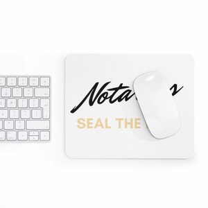 May include: White rectangular mousepad with the words "Notary Seal the" in black and gold lettering. A white wireless mouse rests on the mousepad. A white keyboard is partially visible in the image.