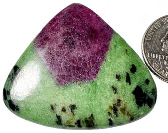 May include: A triangular-shaped gemstone with a vibrant color palette. The stone features a central area of deep red-purple, surrounded by a light green base speckled with black inclusions. A US quarter coin is next to the stone for size comparison.