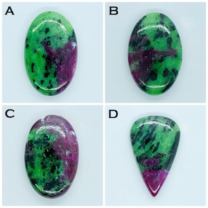 May include: Four polished zoisite gemstones labeled A, B, C, and D. Each stone features a vibrant green base with deep magenta-colored inclusions and scattered black spots. Three stones are oval-shaped, while the fourth is a teardrop shape.