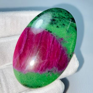 May include: A smooth, oval-shaped green and pink gemstone with a polished finish. The stone has a green top and a pink bottom, with a white band separating the two colors.