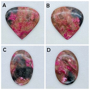 Pode incluir: Quatro pedras preciosas polidas rotuladas A, B, C e D. As pedras A e B têm formato de gota, enquanto C e D são ovais. Cada pedra apresenta um padrão manchado de magenta vibrante, marrom terroso e inclusões minerais pretas profundas.