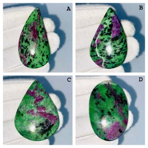 May include: Four polished zoisite gemstones featuring vibrant green backgrounds with distinct inclusions of deep magenta ruby and black hornblende. The collection includes three teardrop-shaped stones labeled A, B, and C, and one oval-shaped stone labeled D.