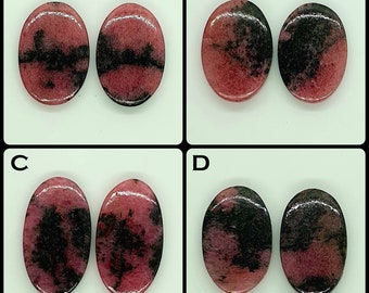 May include: Four pairs of oval-shaped, polished rhodonite cabochons labeled A, B, C, and D. Each stone features a distinct pattern of deep pink and black inclusions, with a smooth, reflective surface and rounded edges, arranged in two columns.