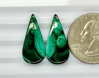 May include: Two green malachite teardrop shaped cabochons with white veining. The cabochons are approximately the size of a US quarter.