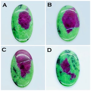 May include: Four oval-shaped polished cabochons labeled A, B, C, and D. Each stone features a vibrant green zoisite base with a prominent, irregular magenta-colored ruby inclusion and scattered black mineral flecks throughout the surface.