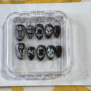 May include: A set of black press-on nails with white skull and crossbones, target, and text designs. The nails are in a clear plastic case with the words "Press On Nails" and "Thank you for your order".