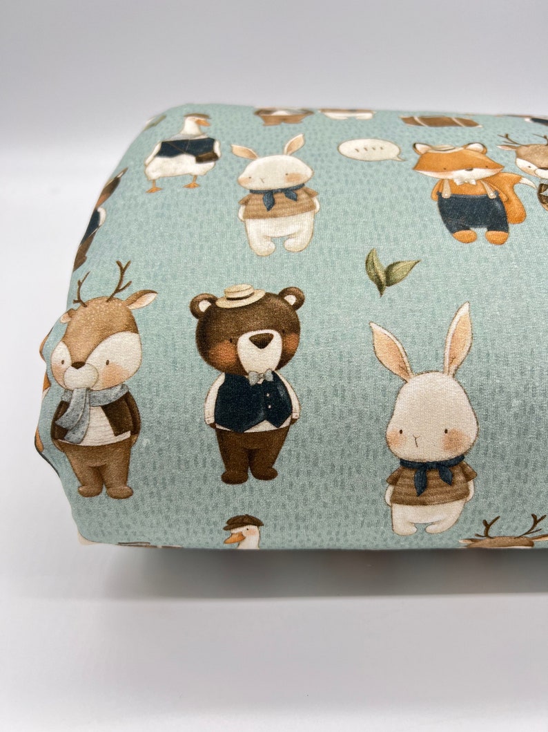 May include: A blue fabric with a repeating pattern of various animals wearing clothing. The animals include a deer, a bear, a rabbit, a fox, and a goose. The animals are all wearing different outfits, including vests, scarves, and hats.