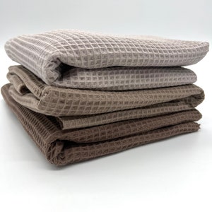 May include: A stack of four waffle weave towels in shades of brown and beige. The towels are folded neatly and are ready to be used.