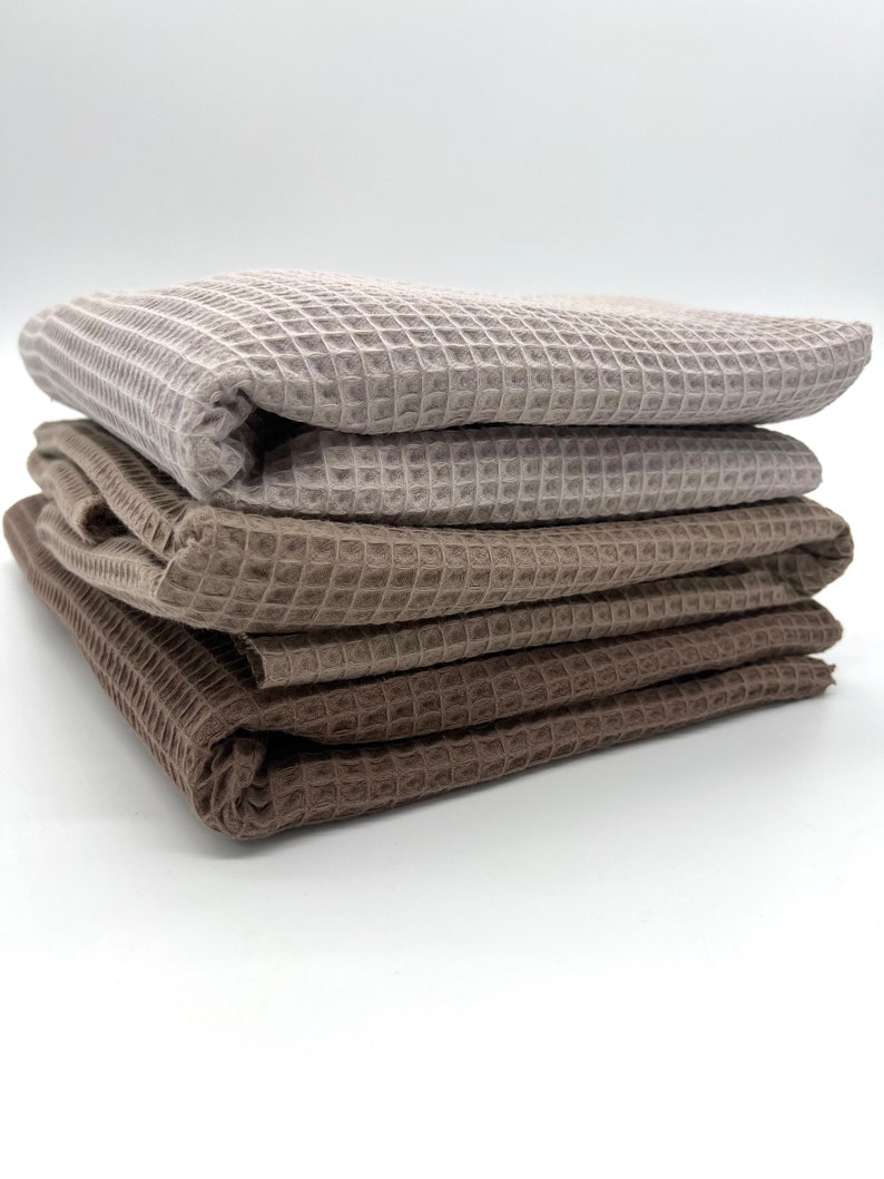 May include: A stack of four waffle weave towels in shades of brown and beige. The towels are folded neatly and are ready to be used.