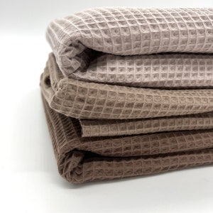 May include: Three waffle weave towels in shades of brown and beige are stacked on top of each other. The towels are folded in half and the edges are visible.