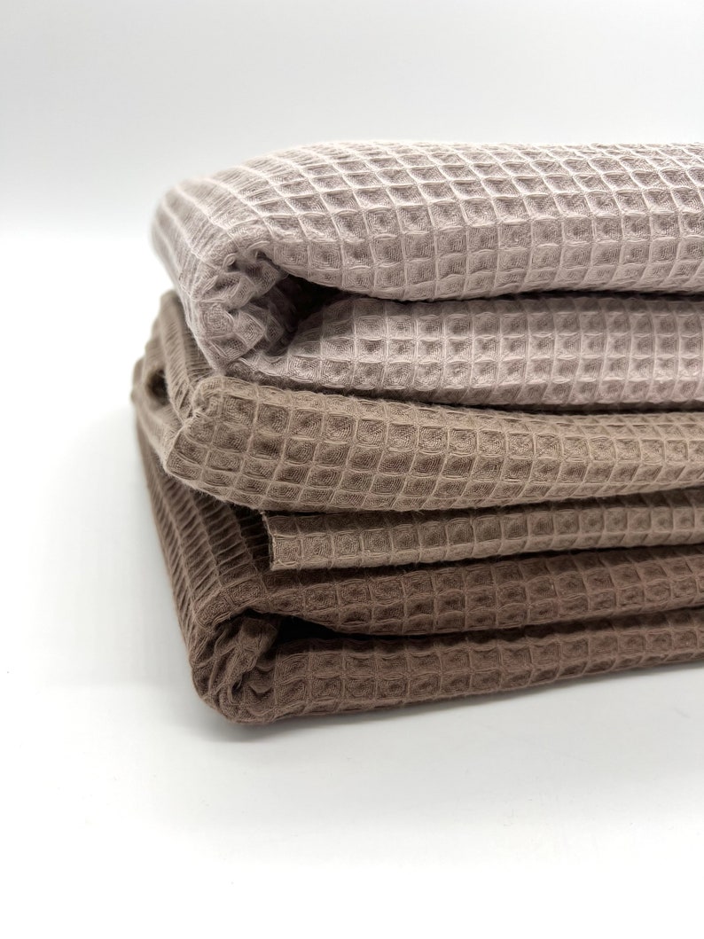 May include: Three waffle weave towels in shades of brown and beige are stacked on top of each other. The towels are folded in half and the edges are visible.
