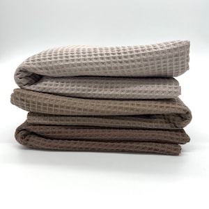 May include: Four waffle weave towels stacked on top of each other. The towels are in shades of brown and beige.