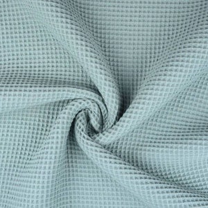 May include: Close-up of a light blue waffle-weave fabric. The fabric is soft and has a textured, grid-like pattern. The fabric is draped and folded, creating shadows and depth. This material is suitable for textiles and home decor.