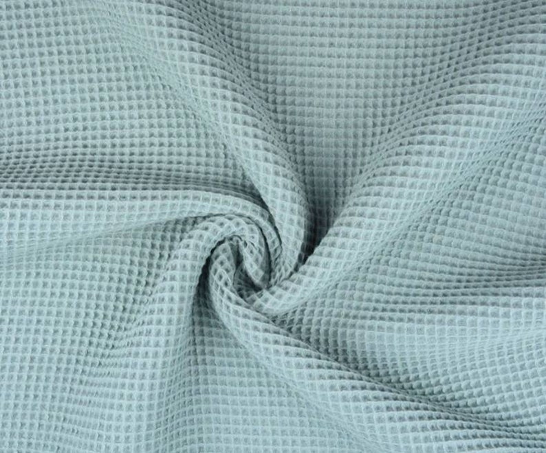 May include: Close-up of a light blue waffle-weave fabric. The fabric is soft and has a textured, grid-like pattern. The fabric is draped and folded, creating shadows and depth. This material is suitable for textiles and home decor.