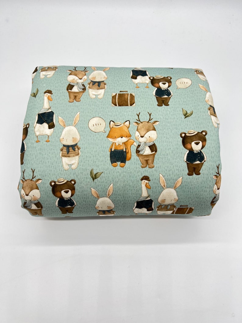 May include: A light blue fabric with a repeating pattern of various animals wearing hats and scarves. The animals include a fox, deer, rabbit, goose, and bear. The fabric has a subtle textured pattern.