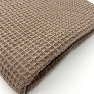 May include: A brown waffle weave fabric folded in half. The fabric has a textured surface and a soft, plush feel.